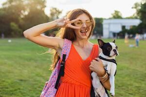 young happy smiling woman in orange dress having fun playing with dog in park photo