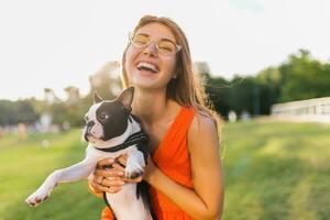 young happy smiling woman in orange dress having fun playing with dog in park photo