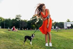 young happy smiling woman in orange dress having fun playing with dog in park photo