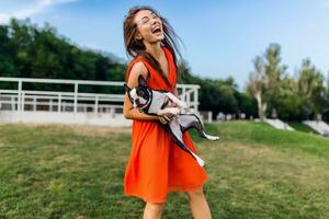 young happy smiling woman in orange dress having fun playing with dog in park photo