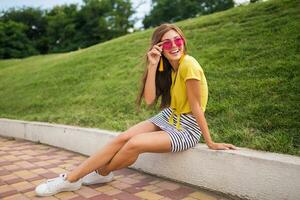 young stylish woman having fun in city park, summer style fashion trend photo