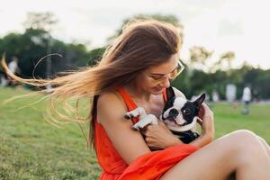 young happy smiling woman in orange dress having fun playing with dog in park photo