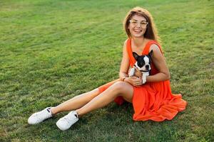 young happy smiling woman in orange dress having fun playing with dog in park photo