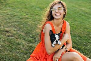 young happy smiling woman in orange dress having fun playing with dog in park photo