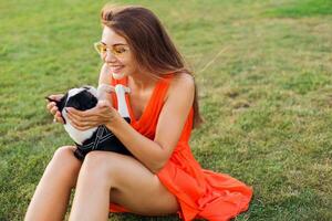 young happy smiling woman in orange dress having fun playing with dog in park photo