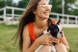 young happy smiling woman in orange dress having fun playing with dog in park photo