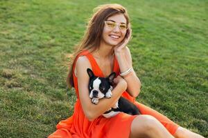 young happy smiling woman in orange dress having fun playing with dog in park photo