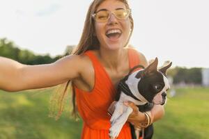 young happy smiling woman in orange dress having fun playing with dog in park photo