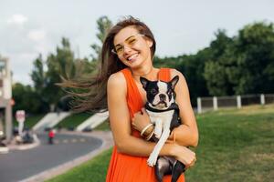 young happy smiling woman in orange dress having fun playing with dog in park photo