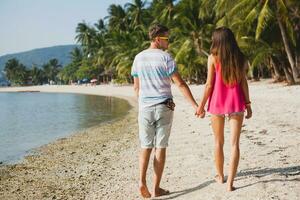 young beautiful couple walking on tropical beach photo