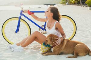 young beautiful woman sitting on sand on beach, holding vintage bicycle photo