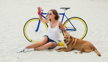 young beautiful woman sitting on sand on beach, holding vintage bicycle photo