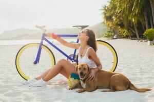 young beautiful woman sitting on sand on beach, holding vintage bicycle photo