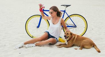 young beautiful woman sitting on sand on beach, holding vintage bicycle photo