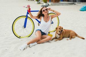 young beautiful woman sitting on sand on beach, holding vintage bicycle photo