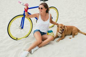 young beautiful woman sitting on sand on beach, holding vintage bicycle photo