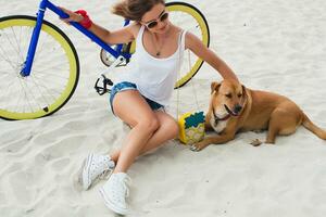 young beautiful woman sitting on sand on beach, holding vintage bicycle photo