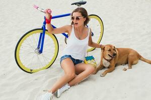 young beautiful woman sitting on sand on beach, holding vintage bicycle photo