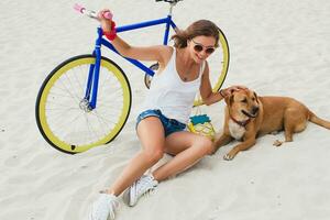 young beautiful woman sitting on sand on beach, holding vintage bicycle photo