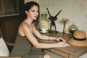 young stylish beautiful woman sitting at table in resort hotel room photo