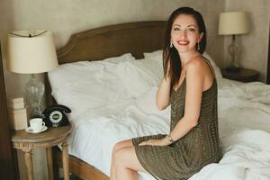 young beautiful woman sitting on bed in hotel room photo