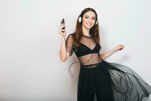 hermosa elegante mujer aislado en negro traje escuchando a música en auriculares bailando foto