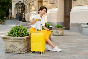 stylish woman traveling with yellow suitcase in Europe photo