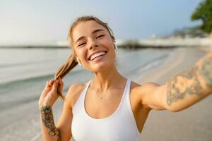 pretty young smiling woman doing sports in the morning in stylish sport outfit sportswear, taking selfie picture on smartphone camera photo