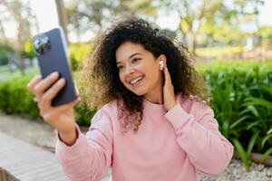 pretty beautiful curly young woman sitting in park using smatphone photo