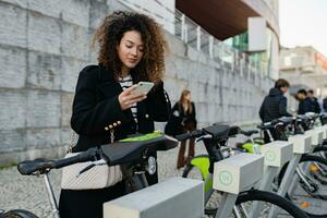 pretty curly woman renting a bicycle in street with an app photo