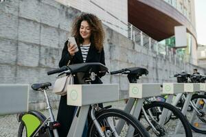 pretty curly woman renting a bicycle in street with an app photo