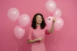 bonito joven mujer posando aislado en rosado estudio antecedentes con rosado aire globos y teléfono inteligente foto