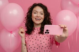 bonito joven mujer posando aislado en rosado estudio antecedentes con rosado aire globos y teléfono inteligente foto