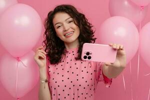 bonito joven mujer posando aislado en rosado estudio antecedentes con rosado aire globos y teléfono inteligente foto