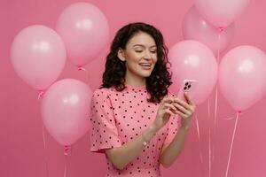 bonito joven mujer posando aislado en rosado estudio antecedentes con rosado aire globos y teléfono inteligente foto