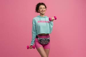 smiling happy beautiful woman in stylish sports outfit doing workout on pink background isolated in studio photo