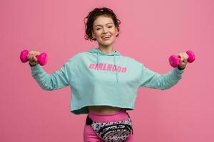 smiling happy beautiful woman in stylish sports outfit doing workout on pink background isolated in studio photo