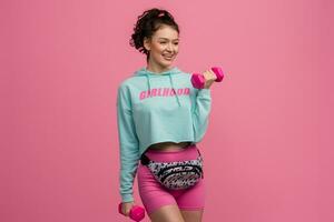 smiling happy beautiful woman in stylish sports outfit doing workout on pink background isolated in studio photo