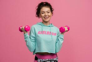 smiling happy beautiful woman in stylish sports outfit doing workout on pink background isolated in studio photo