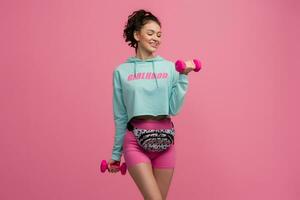 smiling happy beautiful woman in stylish sports outfit doing workout on pink background isolated in studio photo