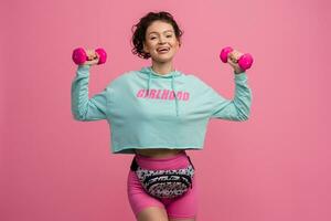 smiling happy beautiful woman in stylish sports outfit doing workout on pink background isolated in studio photo