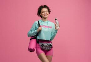 sonriente contento hermosa mujer en elegante Deportes atuendo posando en rosado antecedentes aislado en estudio foto