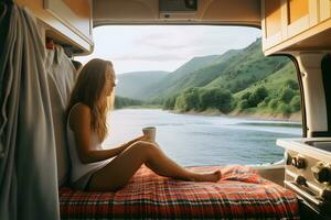 Camper girl holding coffee cup inside camper van at riverside. photo