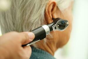 Otolaryngologist or ENT physician doctor examining senior patient ear with otoscope, hearing loss problem. photo