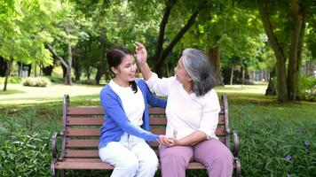 contento mayor madre con gris pelo hablar y risa con hija o cuidador en el parque. concepto de contento Jubilación con cuidado desde un cuidador y ahorros y mayor salud seguro, mayor cuidado video