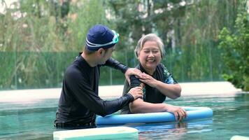 Young trainer helping senior woman in aqua aerobics and working out in the pool. old woman and mature man doing aqua aerobics exercise in swimming pool, Elderly sports, and active lifestyle concept. video