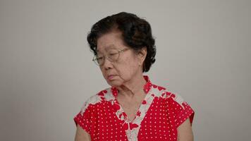 deprimerad asiatisk senior kvinna ensam besviken och tappa bort minne i isolerat vit bakgrund. porträtt gammal kvinna sjuk sjuk depression sjukdom känna ledsen och olycklig, demens, hälsa problem begrepp. video