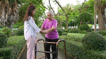 An old elderly Asian woman uses a walker and walking in the garden with her daughter.  Concept of happy retirement With care from a caregiver and Savings and senior health insurance, health care video