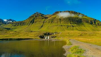 Wonderful waterfall named Kirkjufellsfoss with a Kirkjufell church like iconic mount in Western Iceland, at blue sky and sunny day photo