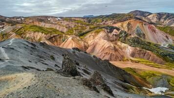 hermoso paisaje islandés panorámico de coloridas montañas volcánicas de arco iris landmannalaugar, en la famosa ruta de senderismo laugavegur con un espectacular cielo nevado y suelo de volcán rojo en islandia. foto